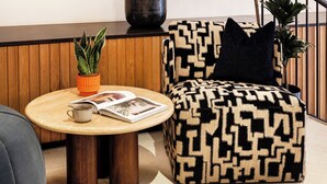 Ein modernes Wohnzimmer mit einem gemusterten Sessel, einem runden Holztisch und mehreren Blumentöpfen.