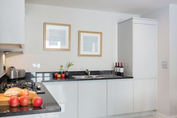 Une cuisine moderne équipée d’une cuisinière à gaz, d’un grille-pain, d’un évier et d’un plan de travail sur lequel sont disposés des fruits et des bouteilles de vin.