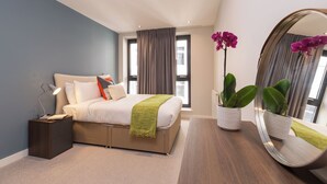 Ein modernes Schlafzimmer mit Bett, Nachttisch, Lampe und zwei Blumentöpfen.