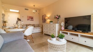 Una sala de estar moderna con sofá, mesa de comedor, televisor y plantas decorativas.