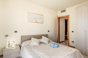 Un dormitorio con cama, mesita de noche, lámpara y un cuadro en la pared.