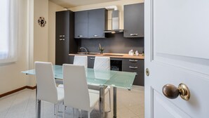 Une cuisine moderne avec des meubles de couleur sombre, une table à manger en verre et des chaises blanches.