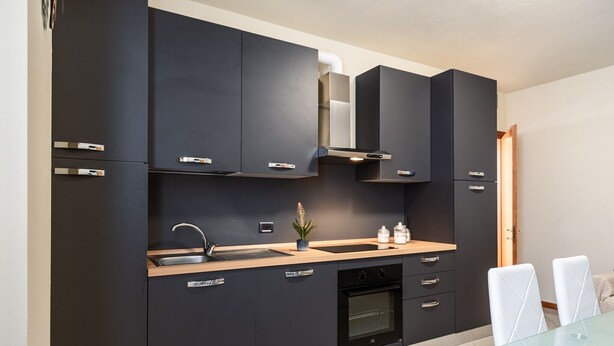 Une cuisine moderne avec des meubles de couleur sombre, un évier en acier inoxydable, un four encastré et une table à manger en verre.