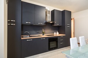 Eine moderne Küche mit dunklen Schränken, einer Edelstahl-Spüle, einem eingebauten Backofen und einem Glastisch.