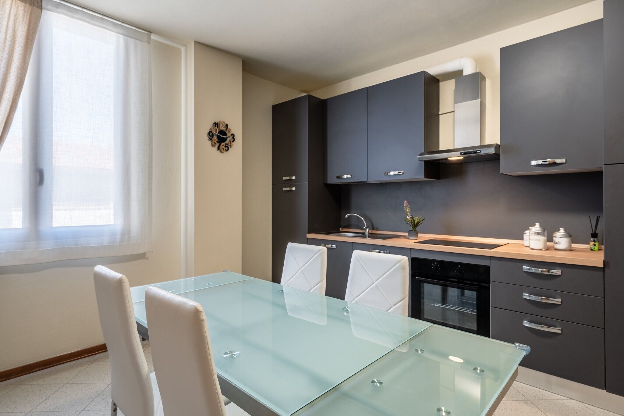 A modern kitchen with dark cabinets, a glass dining table, and a built-in oven.