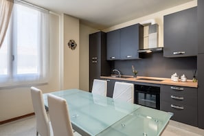 Una cocina moderna con armarios oscuros, una mesa de comedor de vidrio y un horno empotrado.