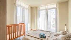 Une chambre à coucher avec un berceau, un lit avec une couette, des oreillers et des rideaux légers.
