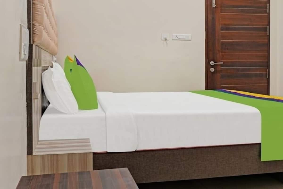 A single bed with a white mattress, a green pillow, and a colorful blanket.