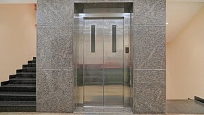 An elevator with a metallic finish, located between two walls with a stone-like texture. - HOTEL JSN GRAND (Vijayawada)