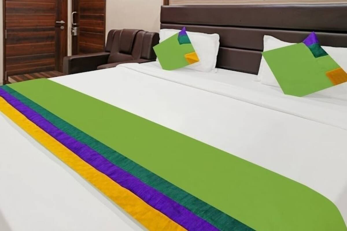 A bed with a rainbow-colored bedspread and two pillows with geometric patterns.