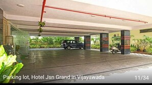 A parking lot at Hotel Jsn Grand in Vijayawada with a black SUV parked, concrete pillars, and potted plants. - HOTEL JSN GRAND (Vijayawada)