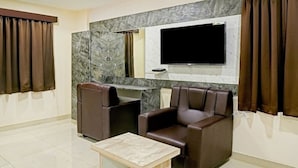 A room with two leather chairs, a small table, a flat-screen TV mounted on a marble wall, and a large mirror. - HOTEL JSN GRAND (Vijayawada)