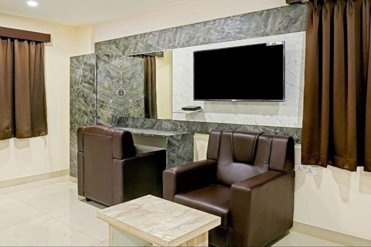 A room with two leather chairs, a small table, a flat-screen TV mounted on a marble wall, and a large mirror.