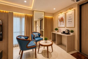 Habitación de hotel con zona de estar, una mesa de centro, una mesita de noche con una planta y una tetera, y un espejo que refleja la habitación.