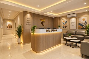 Un mostrador de recepción con un cartel que dice 'RECEPTION', flanqueado por una pared con listones verticales de madera y obras de arte enmarcadas.