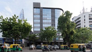 Un edificio moderno con fachada curva, rodeado de árboles y varios vehículos en la calle.