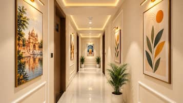 A hallway with framed artwork on the walls, a potted plant, and a staircase at the end.