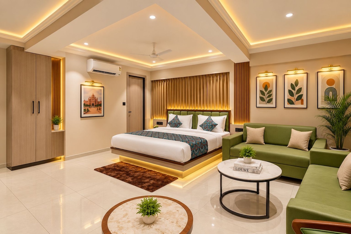 A modern hotel room with a large bed, a green sofa, a round coffee table, and a ceiling fan.