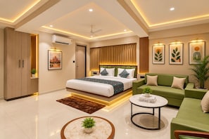 A modern hotel room with a large bed, a green sofa, a round coffee table, and a ceiling fan. - Hotel Royal Time (Ahmedabad)