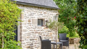 Un bâtiment en pierre avec une petite fenêtre, deux chaises en osier et une table.