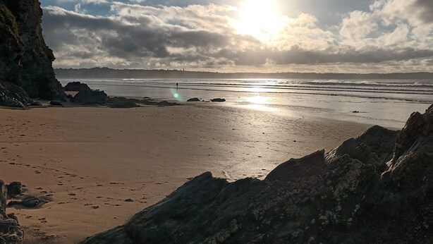 Une plage avec des formations rocheuses, un ciel dégagé et un soleil éclatant.
