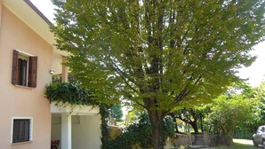 A residential building with a tree in front, a covered patio, and a parked car. - Villa Rosa Apartment (Borso del Grappa)
