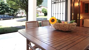 A wooden table with a wicker basket containing a sunflower and vegetables, two wooden chairs, and a view of a parked car and greenery outside. - Villa Rosa Apartment (Borso del Grappa)