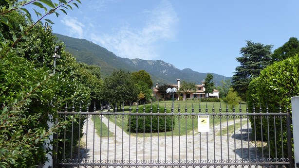 A gated property with a paved driveway leading to a building with a mountain backdrop. - Villa Rosa Apartment (Borso del Grappa)