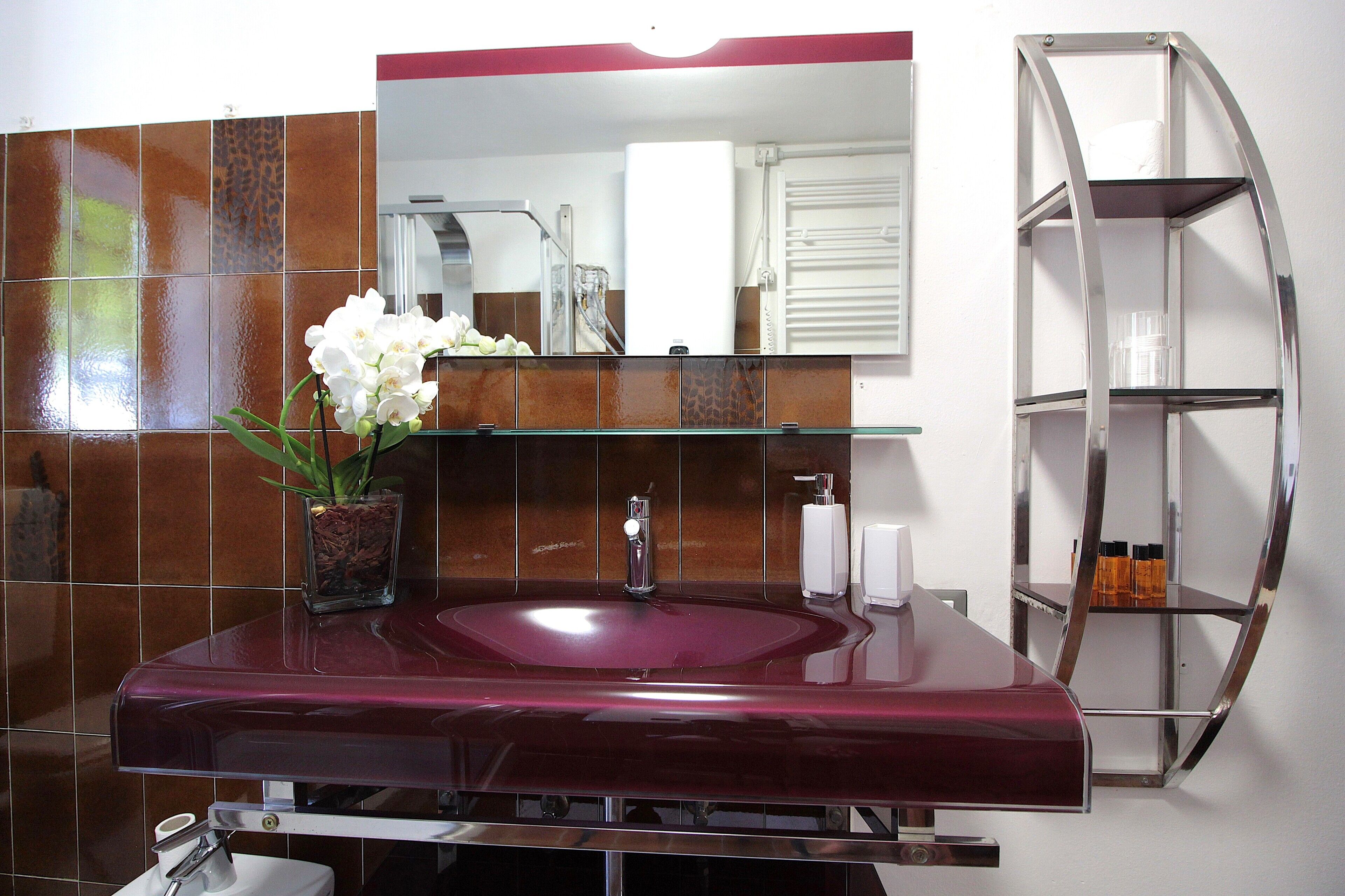 A bathroom with a marble sink, a glass vase with flowers, a mirror, and a chrome shelf.