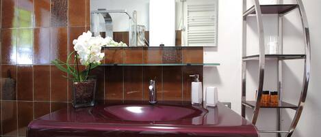 A bathroom with a marble sink, a glass vase with flowers, a mirror, and a chrome shelf.