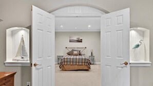 A bedroom with a bed, a nightstand, a dresser, and a window with a bird sculpture.