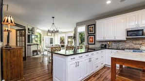A spacious kitchen with white cabinetry, a central island, and a dining area with wooden chairs.
