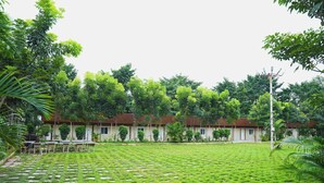 A courtyard with a lawn, a building with a red roof, and surrounding greenery. - Golden Farms Resorts (Anekal)