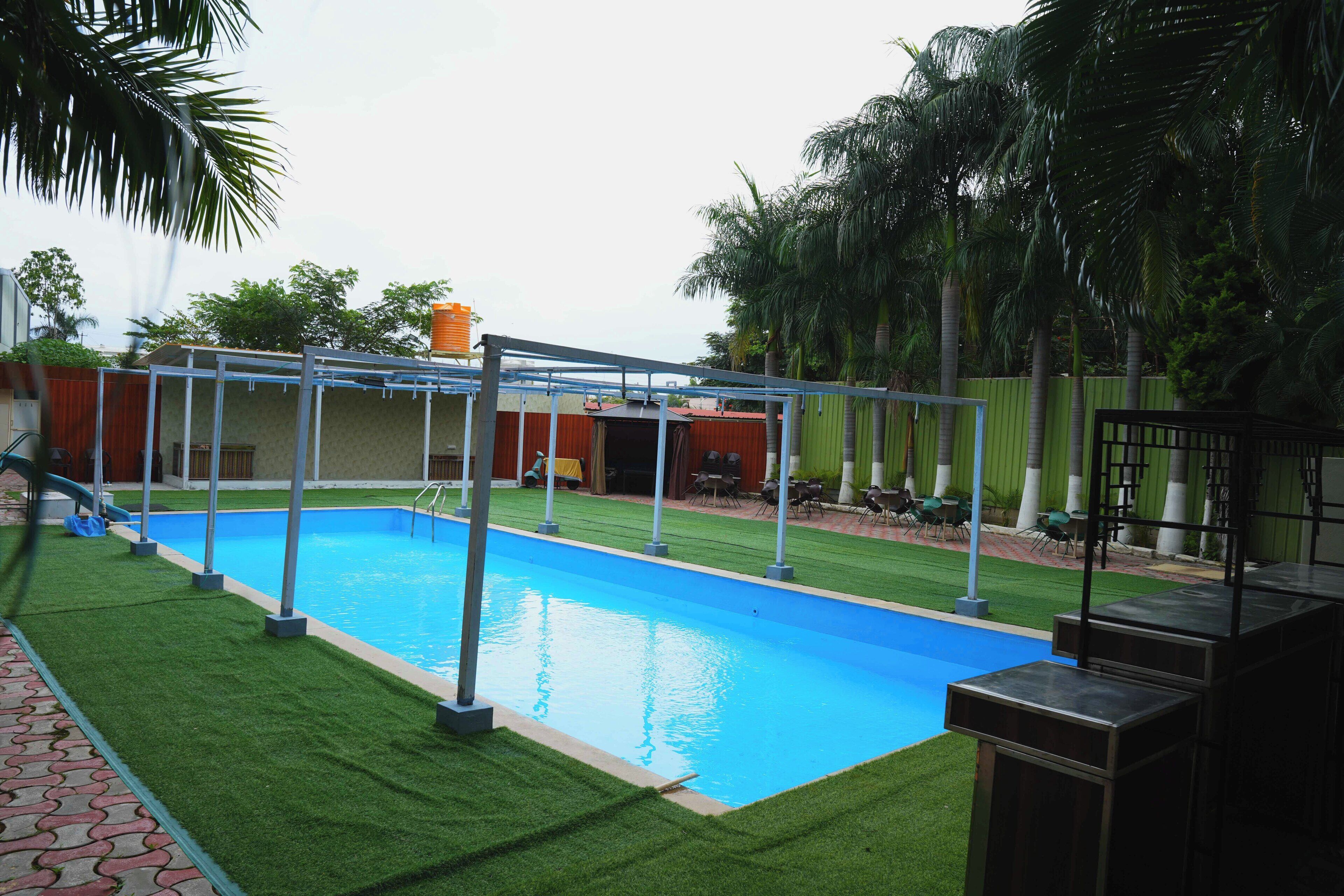A rectangular swimming pool with a metal frame, surrounded by artificial grass, and a covered area with a roof.