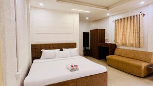 A modern hotel room with a large bed, a sofa, a wardrobe, and a ceiling fan. - Golden Farms Resorts (Anekal)