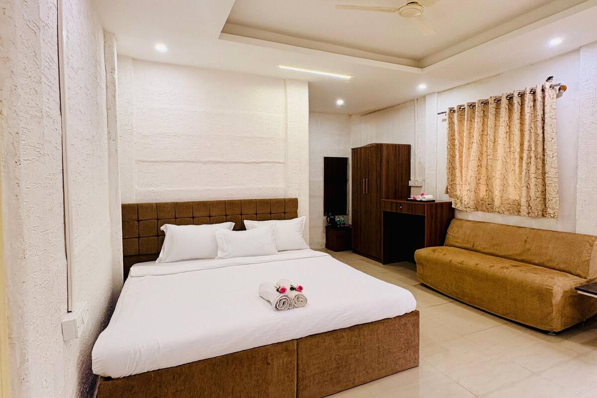 A modern hotel room with a large bed, a sofa, a wardrobe, and a ceiling fan.