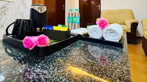 A hotel room with a marble countertop, a coffee machine, a tray with black mugs, a bottle of water, a towel, and a pink rose. - Golden Farms Resorts (Anekal)