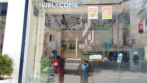 A storefront with a glass facade, a 'WELCOME' sign, and a 'Cold Coffee' sign. - Mandakini River View (Jakholi)