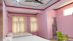 A room with two beds, a ceiling fan, a green chair, and a table with a remote control. - Mandakini River View (Jakholi)
