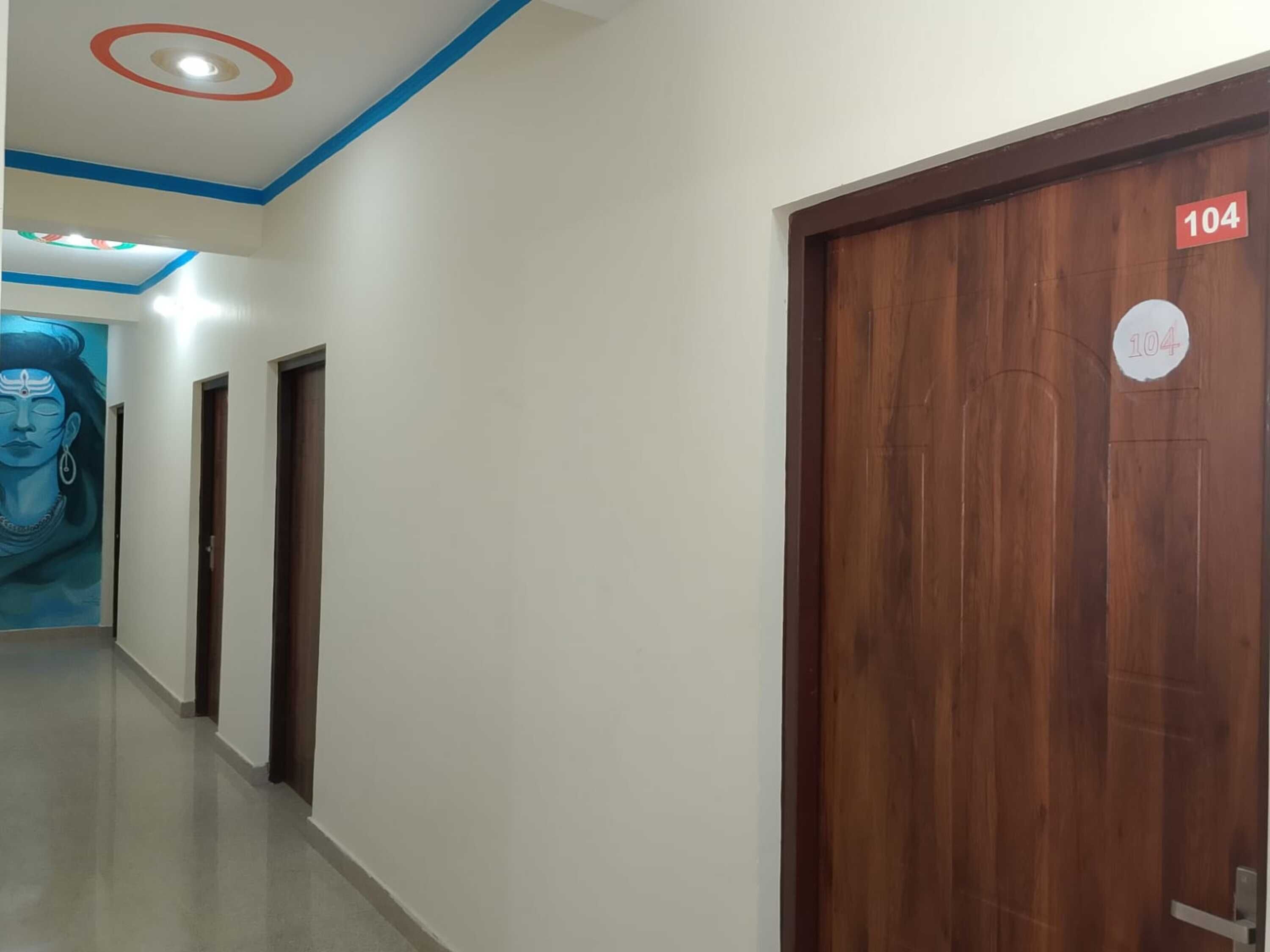A hallway with a wooden door marked 104, a blue and white ceiling with recessed lighting, and a mural on the wall.
