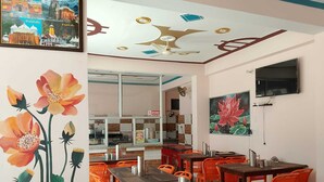 A dining area with orange chairs and tables, a kitchen in the background, and a ceiling with a star design. - Mandakini River View (Jakholi)