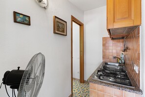 A kitchen with a gas stove, a fan, and a door leading to another room.