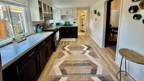 A modern kitchen with dark cabinets, a central island, and a patterned rug. - Wild Bird Grove – Paws Welcome, Near Downtown SLC (Salt Lake City)