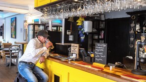 Una zona de bar con mostrador, menú en pizarra y vasos colgantes.