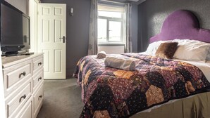 Un dormitorio con cama, cómoda, televisor y ventana con cortinas.