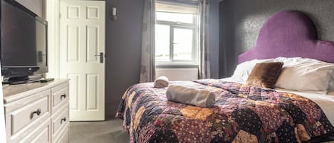 A bedroom with a bed, a dresser, a television, and a window with curtains.