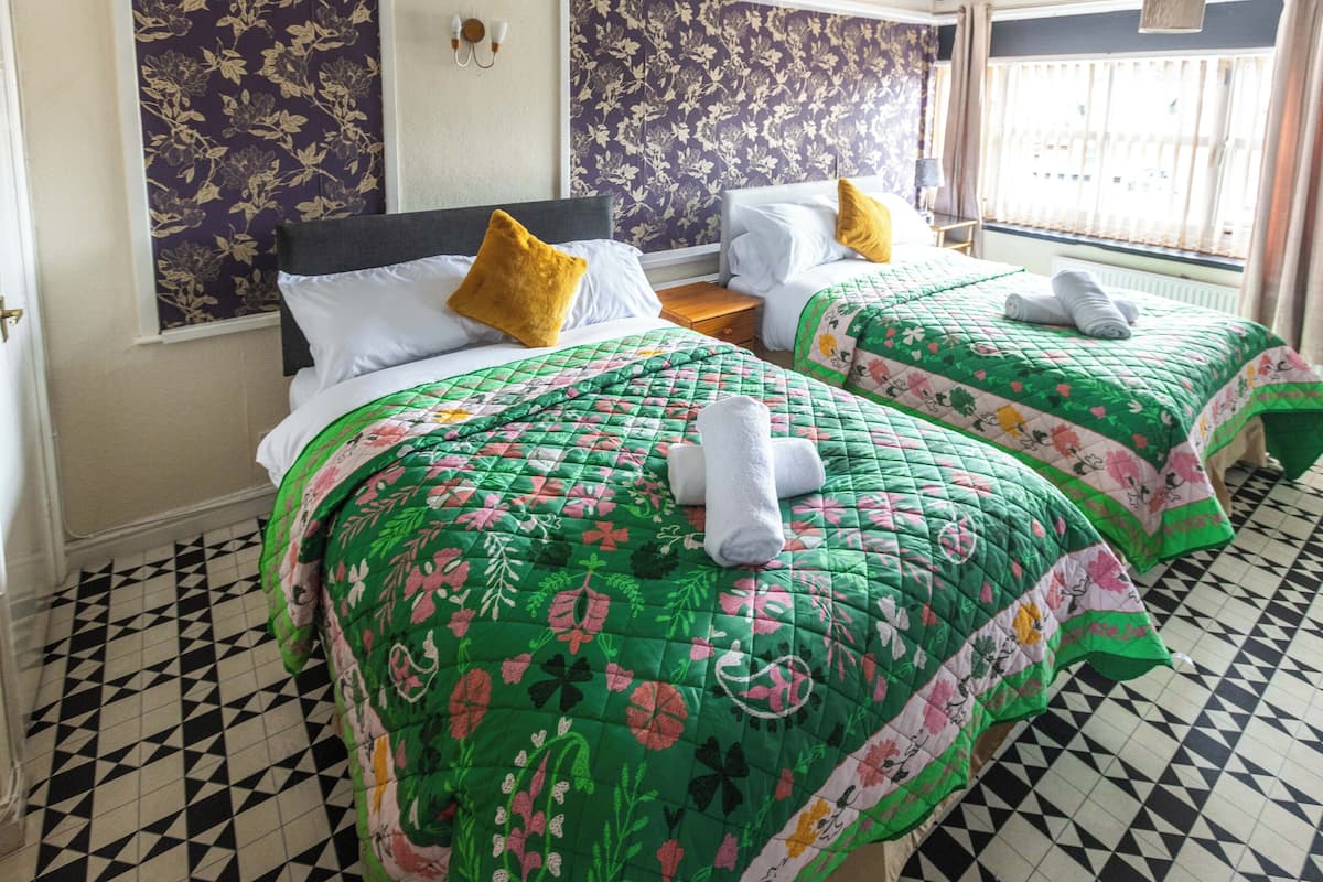 Een hotelkamer met twee bedden, bloemenbehang, een geruit vloertje en een raam met gordijnen.