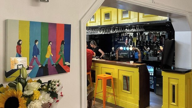 Zona de bar con armarios amarillos, una barra y una persona trabajando detrás.