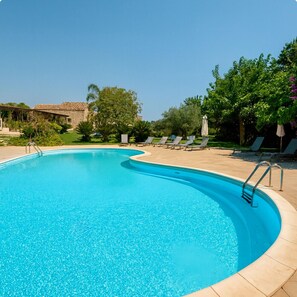 Une piscine d’un bleu éclatant, à bords incurvés, entourée de chaises longues et de parasols.