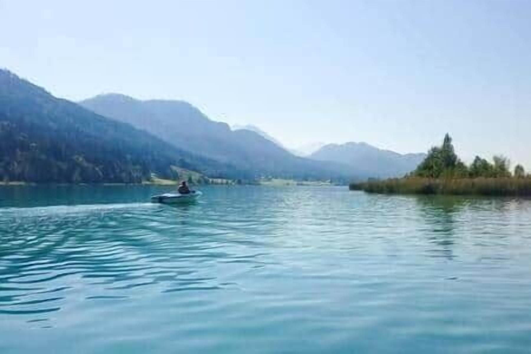 Ein ruhiger See mit einem einzelnen Boot, umgeben von Bergen und Vegetation.